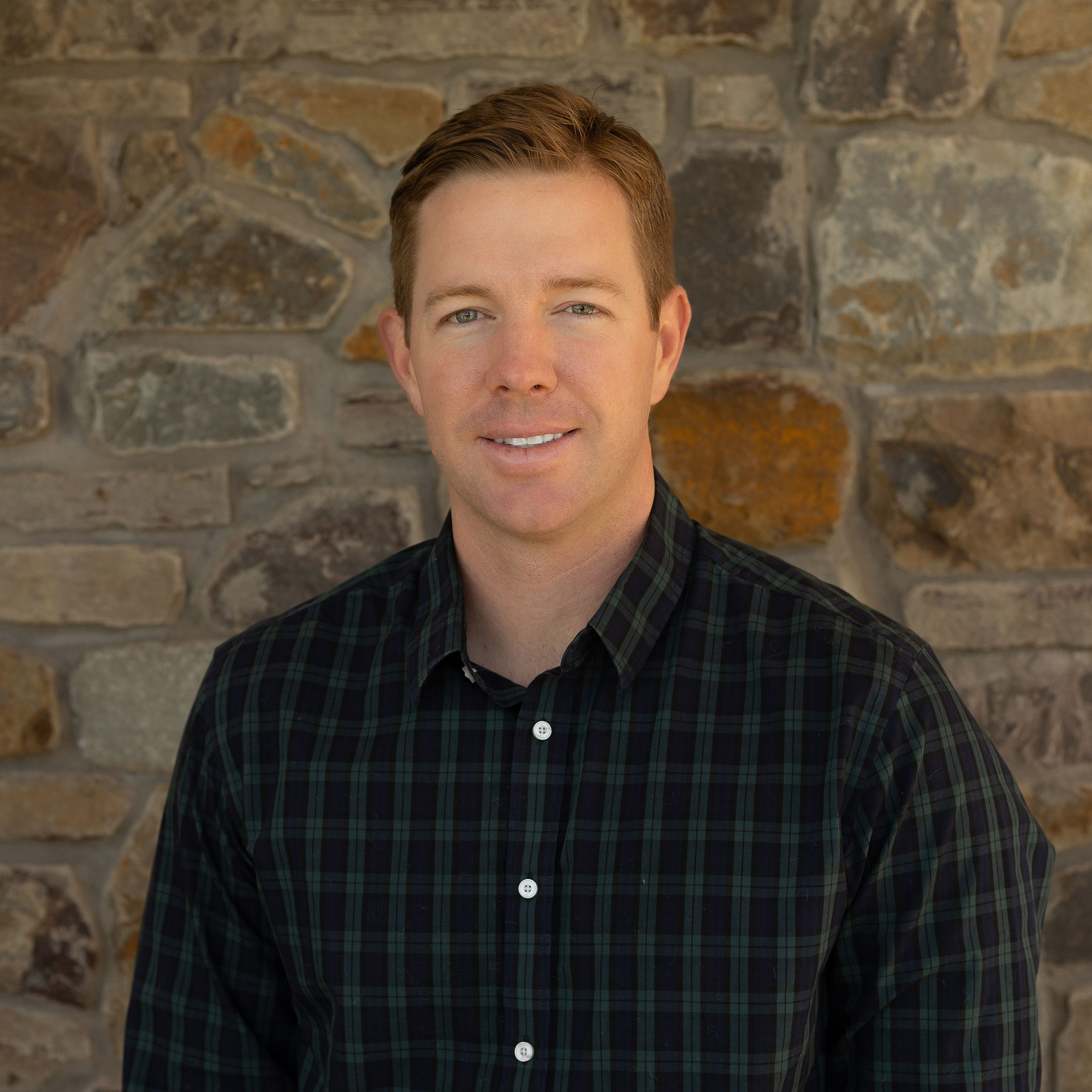 Person in plaid shirt, stone wall background.