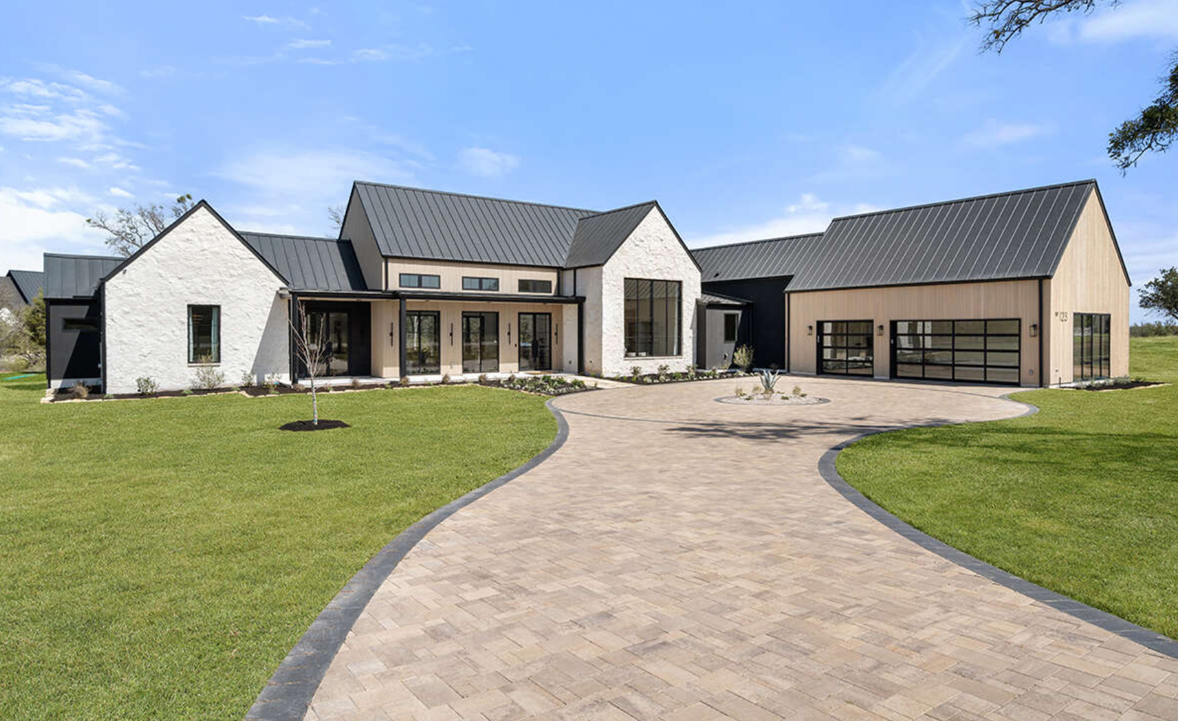 Modern farmhouse with large driveway and green lawn.